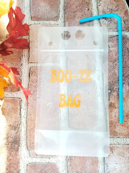A clear plastic drink pouch with orange vinyl design, labeled 'BOO-ZE BAG', displayed on a brick surface with autumn leaves around.