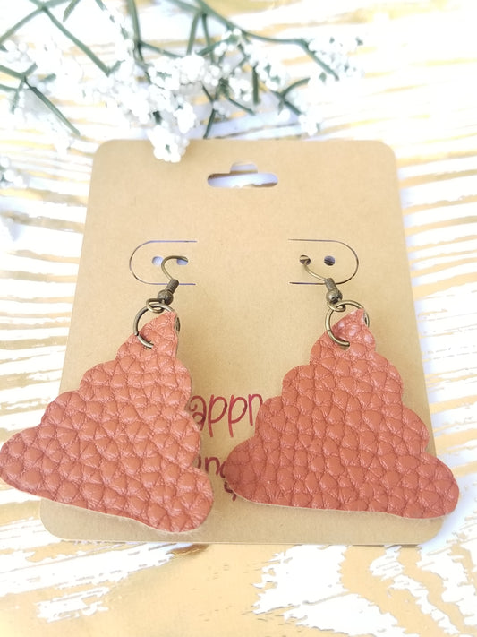 A pair of brown-colored, faux leather earrings shaped like poop, presented on a hanger with a floral background.